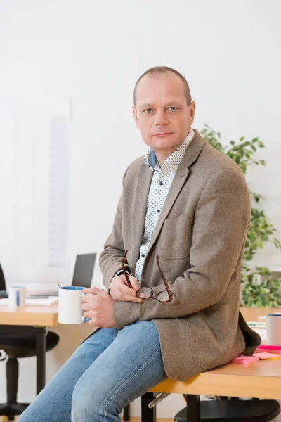 Porträtt Mogen Entreprenör Hålla Kaffekoppen Och Glasögon Medan Sitter Skrivbord — Stockfoto