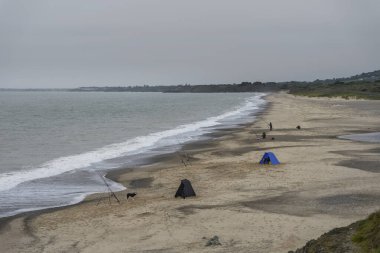 Dengesiz bir İrlanda sahilinde sörf yapan balıkçılar, yoğun gri gökyüzünün altında, sonbahar sahnesinde dalgalı denizlere hat döşüyorlar..
