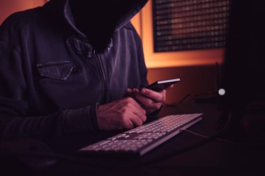 Bilgisayar korsanı karanlık iç, düşük anahtar seçici odak ile smartphone aygıt kullanma