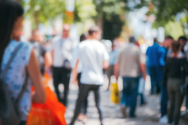 Abstract blurry background, people walking on crowded street on sunny summer day. Defocus blurred background as graphic design element.