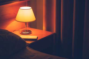 Otel odasında gece masada kitap ve vintage lamba. Retro tarz yatak odası iç.