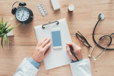 Bir erkek doktor hastane ofisinde muayene sırasında Notlar, hastanın tıbbi geçmişini veya ilaç reçete Pano kağıda yazı havai görünümü
