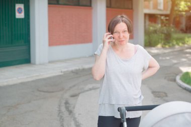 Cep telefonu üzerinde konuşurken ve rahat spor giyim sokakta yürürken bir bebek arabası bebek iterek mutlu anne