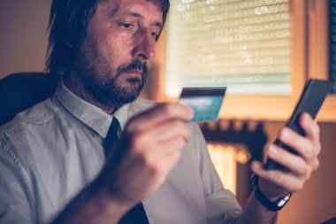 Mobil Bankacılık kullanarak işadamı kredi kartı ve karanlık ofis iç, seçici odak smartphone ile online satın almak için app Hizmetleri