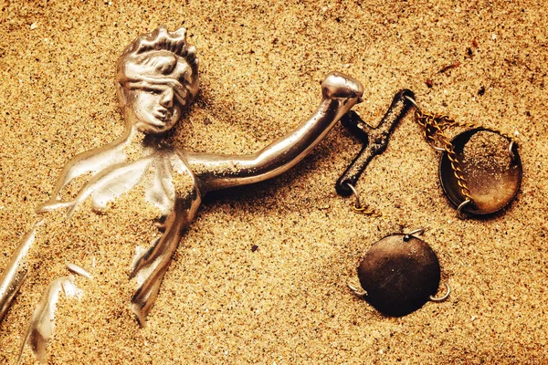 Statue of lady Justice with scale buried in sand, concept of unsolved cold case crime