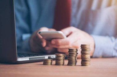 Smartphone ile kullanarak işadamı paralar ön planda yığılmış, seçici odak ile atış kadar yakın