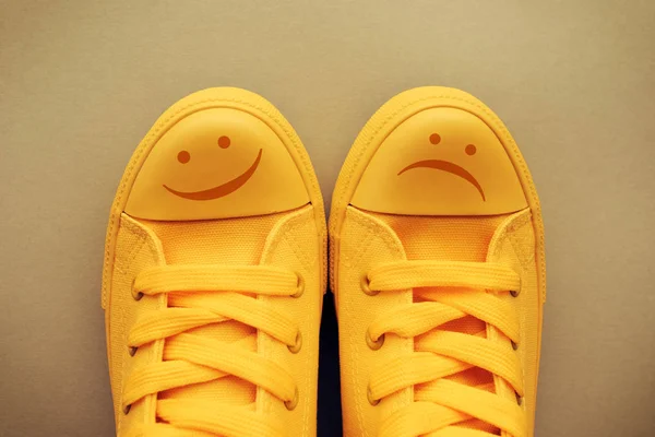 Happy and sad smiley emoticon symbol on yellow sneakers, conceptual image for feelings and emotions of young person and teenage mood swings