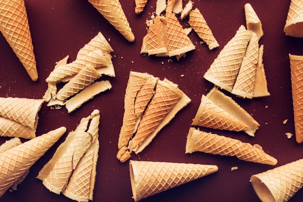 Crushed ice cream waffle cones on dark brown background, flat lay