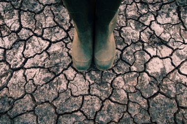 Çiftçi kauçuk kuru toprak zeminde ayakta bot, küresel ısınma ve iklim değişikliği büyüyen bitkileri ve verimi etkileyen