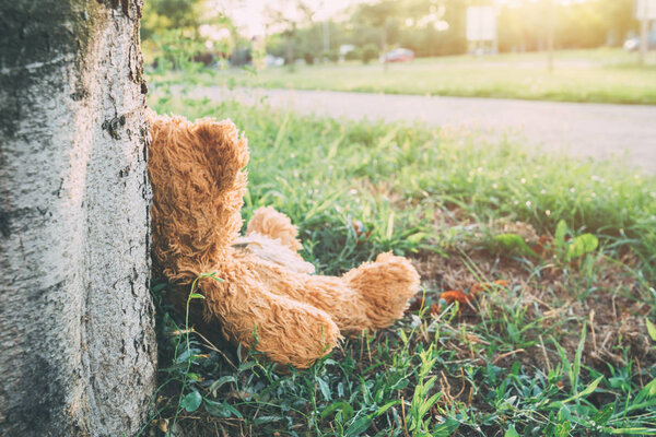 Miserable abandoned teddy bear outdoors leaning on to tree