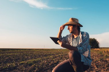 Tarımsal üretim planlama ve hazırlık modern teknoloji kullanan günbatımı, ciddi kendine güvenen adam çıplak boş alanında tablet bilgisayar ile çiftçi ziraat mühendisi