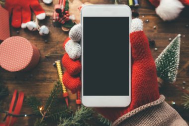 Noel sezonu kadar alay etmek için elinde Smartphone ile arka planda şenlikli tatil dekorasyon.