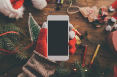 Noel sezonu kadar alay etmek için elinde Smartphone ile arka planda şenlikli tatil dekorasyon.