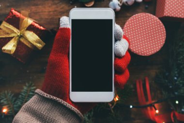 Noel sezonu kadar alay etmek için elinde Smartphone ile arka planda şenlikli tatil dekorasyon.