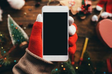 Noel sezonu kadar alay etmek için elinde Smartphone ile arka planda şenlikli tatil dekorasyon.