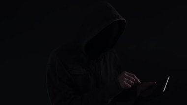 Kukuletalı bilgisayar korsanı ile dijital tablet siber suçlar ve cybersecurity kavramı, düşük anahtar yavaş hareket kullanma yüzünü kapatmamasını