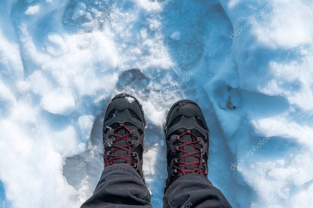 Male feet in boots standing in pure winter snow, top view
