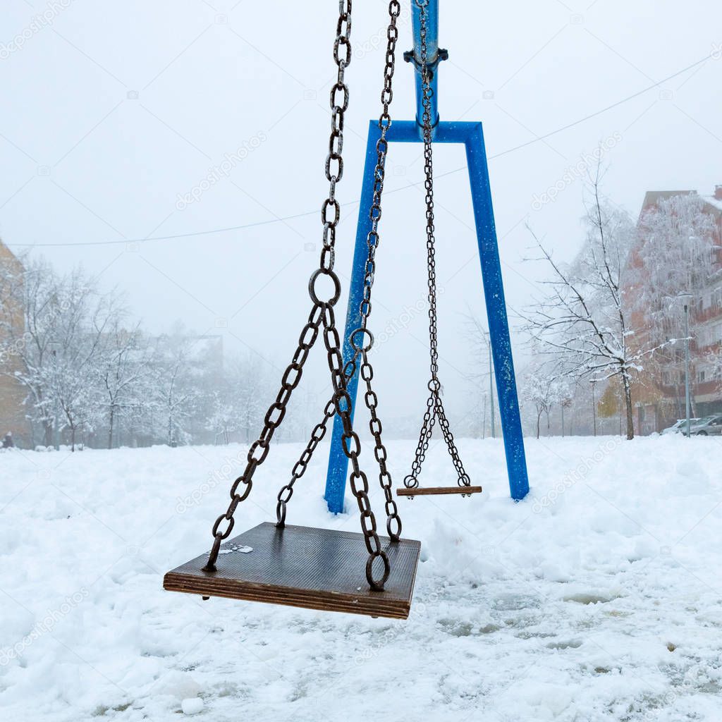 Empty swing in winter with snow covering children's playground