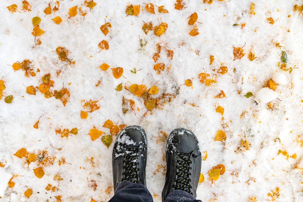 Male feet in boots standing in winter snow covered with yellow leaves