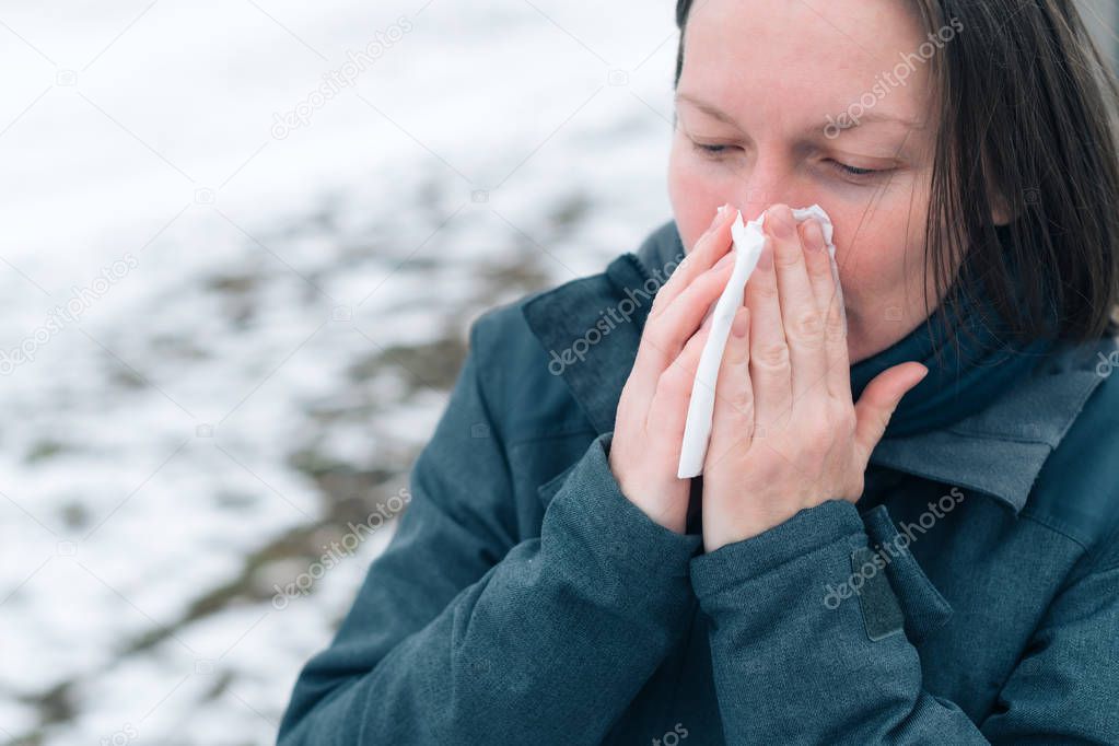 Woman blowing her nose into paper handkerchief out on the street on a cold winter day at the start of the flu season