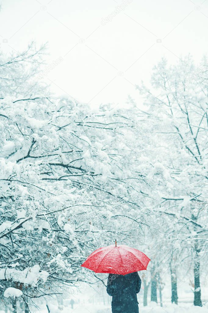 Woman under red umbrella in snow enjoying the first snowfall of the winter season