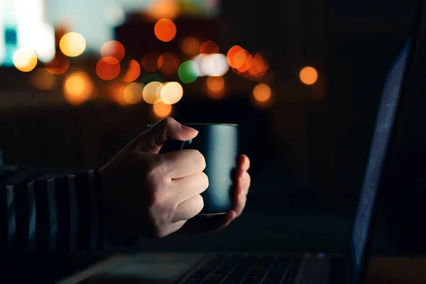夜では ラップトップ コンピューターを見てコーヒー カップを持つ女性は 手のクローズ アップ — ストック写真