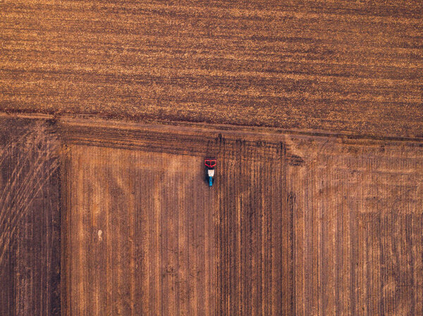 Вид с воздуха на сельскохозяйственный трактор, делающий стерню в поле, вид сверху с беспилотника
