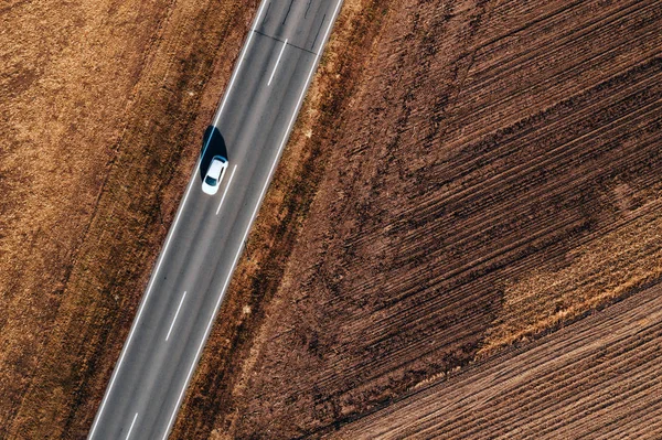 Aerial view of cars driving on the road through plain countryside on sunny autumn afternoon from drone pov.