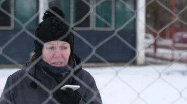 Hayal kırıklığına uğramış kadın cep telefonu engel soğuk kış gününde, seçici odak sembolize zincir bağlantı çit arkasındaki sokakta söz
