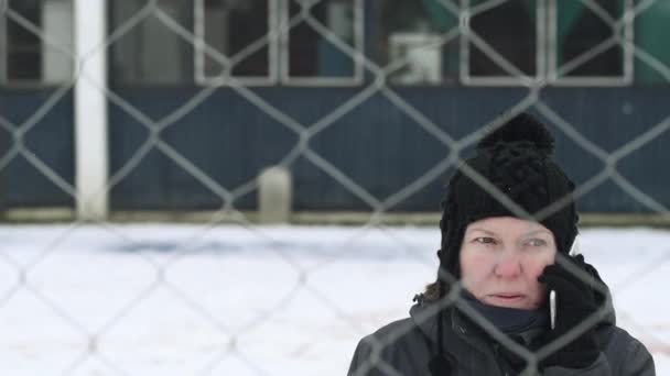 冬の寒い日 選択と集中の障害を象徴する金網フェンスの後ろに通りに携帯電話で話している問題を抱えた女性 — ストック動画