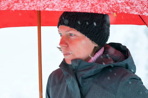 Sad disappointed woman in standing in winter snow under big red umbrella