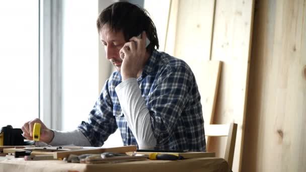 在他的小型木工作坊里 男木匠在用手机说话 — 图库视频影像