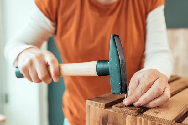 Female carpenter hammering nail into wooden crate — Stock Photo, Image