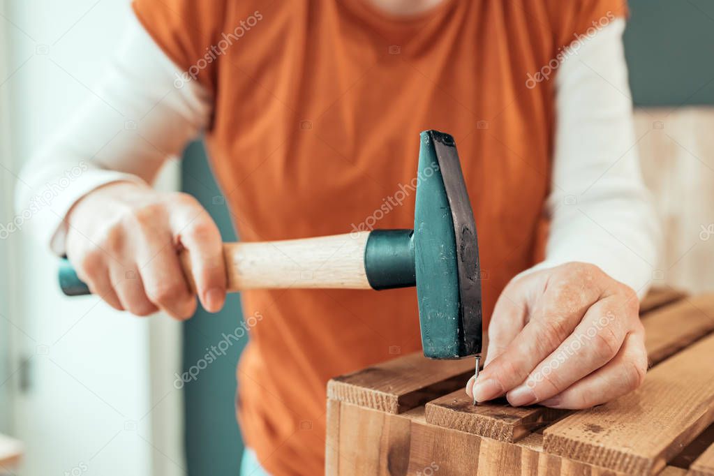 Female carpenter hammering nail into wooden crate