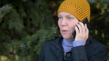 Neşeli kadın cep telefonu dışarı parkta yeşil çam ağacı önünde konuşurken sarı şapkası
