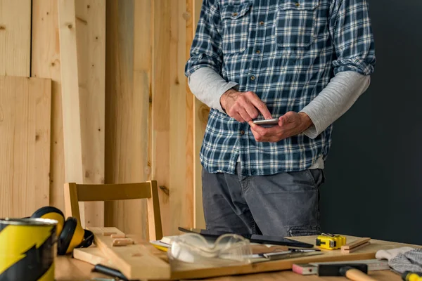 Tischler mit Smartphone in kleiner Holzwerkstatt — Stockfoto