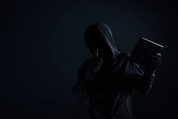 Hooded datorhackare med skyms ansikte med hjälp av digitala tablett — Stockfoto