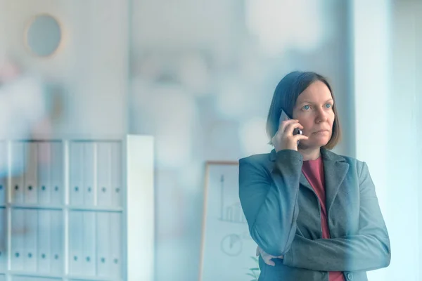 Серьёзная деловая женщина разговаривает по мобильному телефону в офисе — стоковое фото