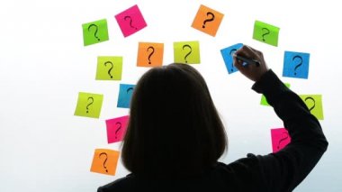 İşkadını renkli yapışkan not kağıdına office beyaz tahta üzerinde soru işaretleri yazma