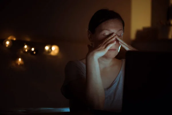 Tired woman working overtime on laptop computer at night