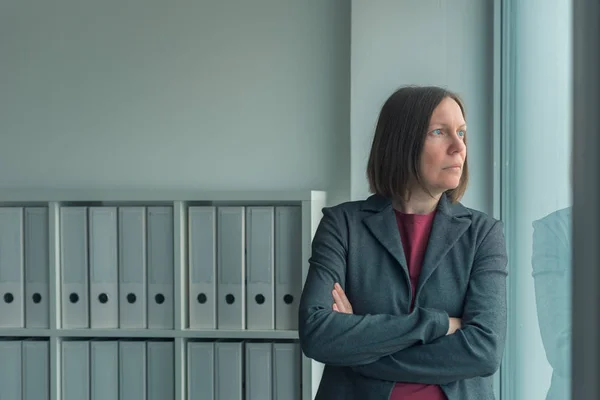 Donna d'affari preoccupata che guarda fuori dalla finestra dell'ufficio — Foto Stock