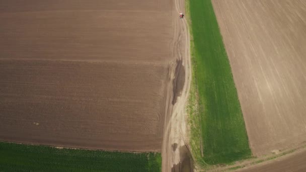 フィールドに向かう田舎の泥道に付属の作物噴霧器を持つトラクターの航空写真 — ストック動画