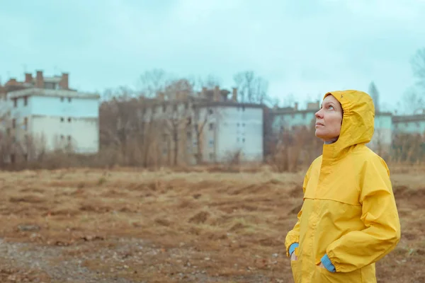 Frau in gelbem Regenmantel blickt auf regnerische Wolken — Stockfoto