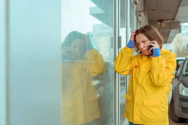 Mulher triste em capa de chuva amarela falando no celular — Fotografia de Stock