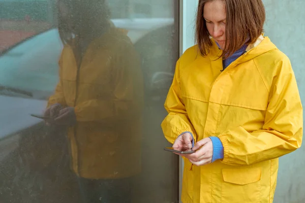 Mulher em capa de chuva amarela mensagens de texto no celular ao ar livre — Fotografia de Stock
