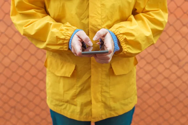 Mujer en impermeable amarillo mensajes de texto en el teléfono móvil al aire libre —  Fotos de Stock