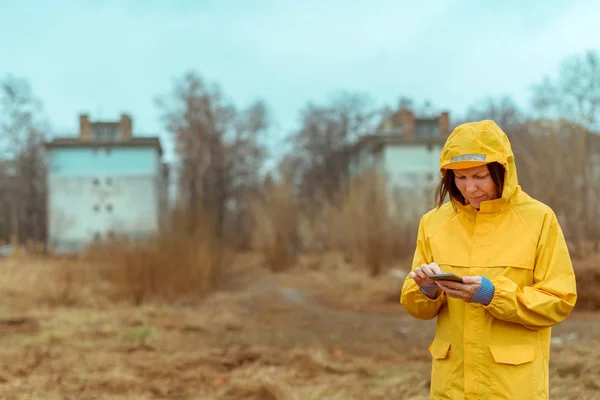 Femme en imperméable jaune textos sur téléphone mobile à l'extérieur — Photo