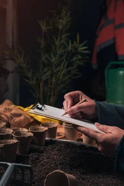 Trädgårdsmästare skriva anteckningar på Urklipp anteckningspapper — Stockfoto