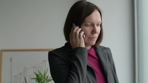 Ciddi Kadını Ofiste Cep Telefonuyla Konuşuyor Pencereden Dışarı Bakıyor — Stok video
