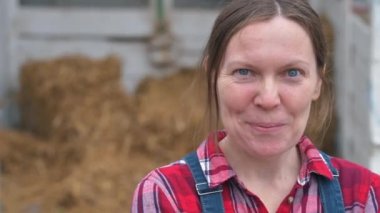 Gülümseyen kadın çiftçi çiftlikte poz. Kendine güvenen kadın çiftlik işçisi kamera bakıyor ekose gömlek ve kot tulum giyiyor